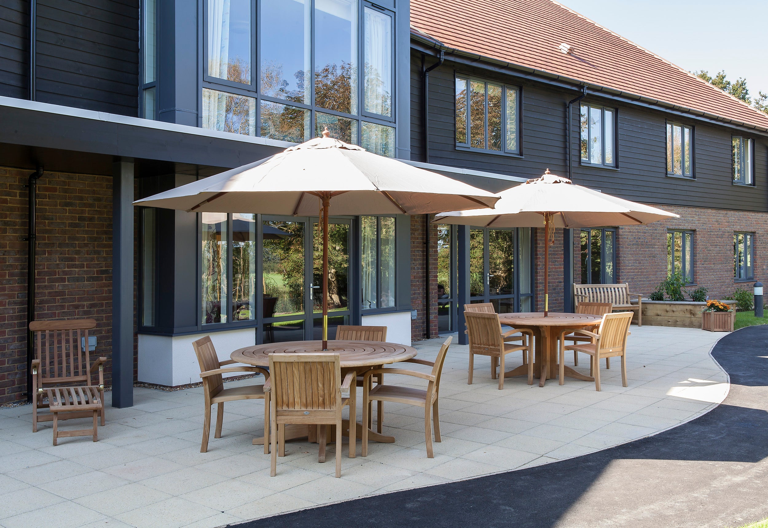 Alexander Rose Commercial Roble round table and chairs with open parasol in an outdoor setting