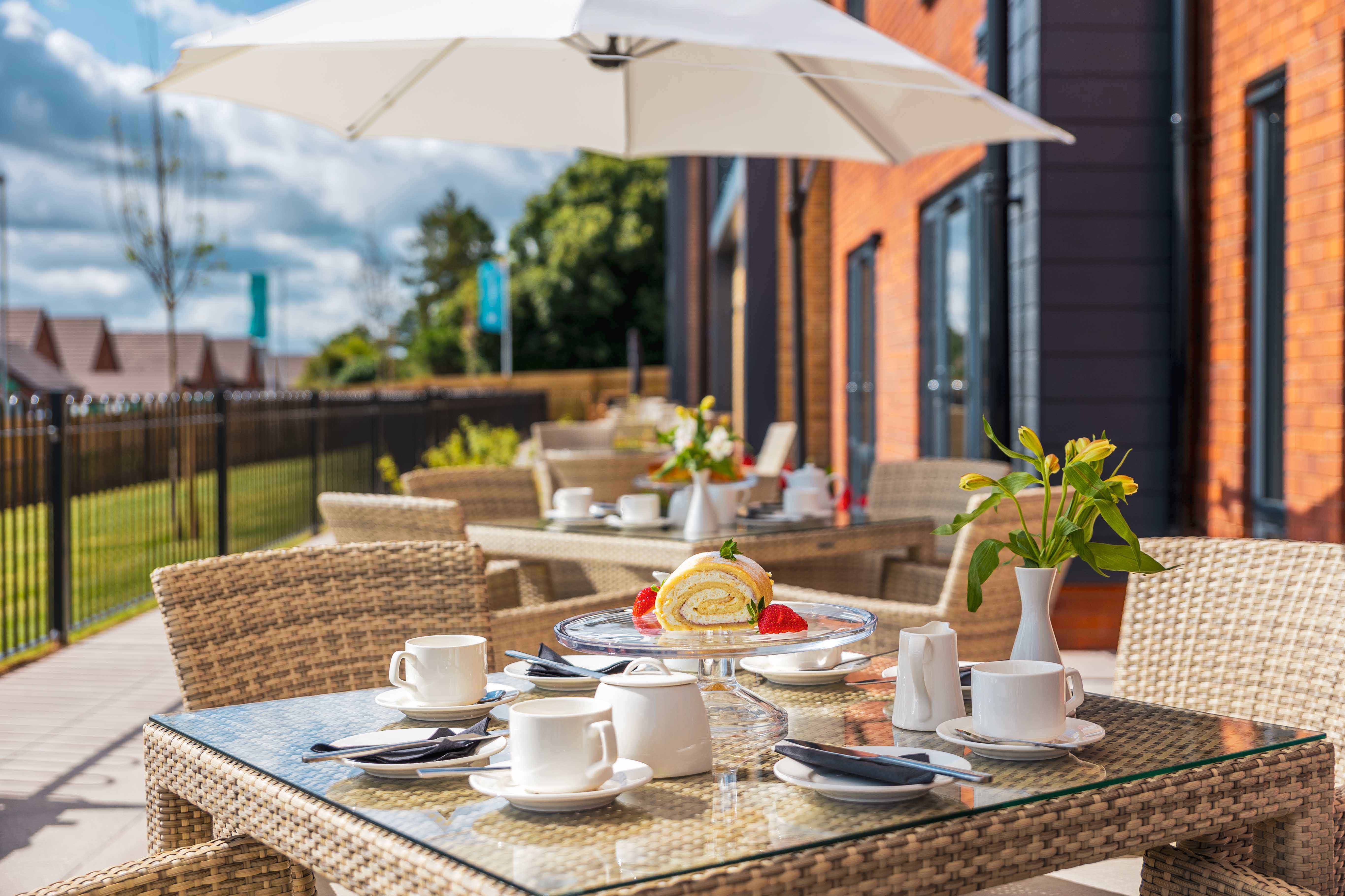 Barchester Elgar Court with Bespoke Alexander Rose Commercial weaved garden furniture and parasol displaying a tea party